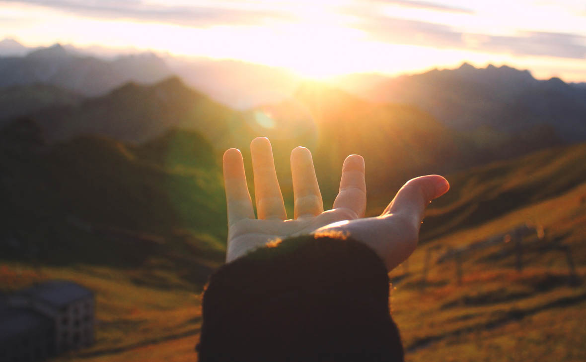 Hand reaching to the sky with setting sun in background
